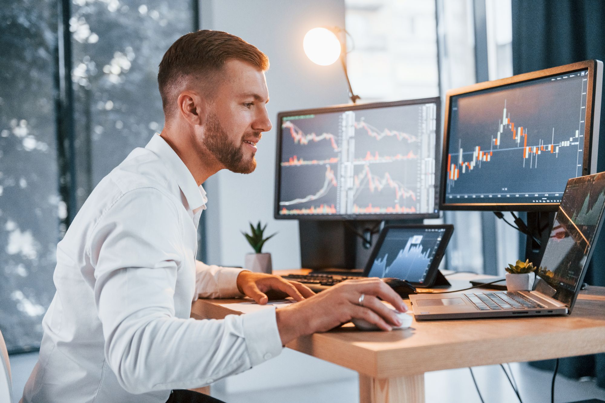 Stock market. Young businessman in formal clothes is in office with multiple screens.